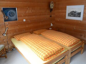 Ein Zimmer in einer Holzhütte mit einem Bett, einer Lampe, einer Uhr und zwei gerahmten Bildern.