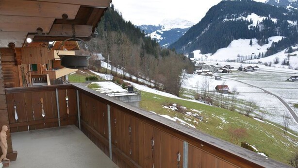 A wooden balcony with a view of a snowy landscape and mountains.