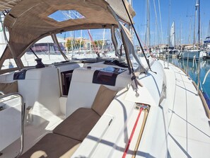 A boat's interior with a cushioned seating area, a steering wheel, and a view of a marina with multiple boats. - Sun-Kissed Sailing Adventure in the Ionian Islands, Lefkada (Lefkada)