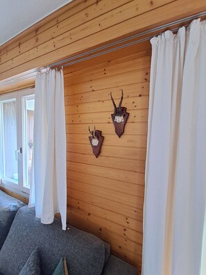 Ein Zimmer mit Holzvertäfelung, zwei aufgehängten Tierkopfskulpturen, einem grauen Sofa und weißen Vorhängen.