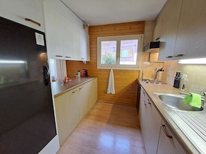 A compact kitchen with wooden paneling, a window, and a stainless steel sink. - Bergluft Appartement/Fewo, Dusche oder Bad, WC 6-Bettwohnung by Interhome (Zweisimmen)
