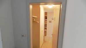 Un estrecho pasillo con un extintor a la izquierda, que conduce a una habitación con una puerta y una estantería llena de libros.