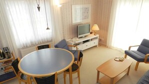 Una sala de estar con una mesa redonda, dos sillas, un sofá, un televisor y una lámpara.