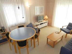 Ein Wohnzimmer mit rundem Tisch, zwei Stühlen, einem Sofa, einem Fernseher und einer Lampe.