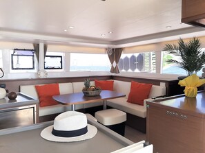 A boat interior with a dining area, seating, and a view of the sea. - Sun-Kissed Sailing Adventure in the Ionian Islands (Mpenitses)