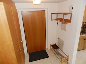 A hallway with a wooden door, a small bench, a black mat, and a shelf with hanging items. - Diamant Appartement/Fewo, Dusche oder Bad, WC, 1 Schlafraum 2-Bettwohnung by Interhome (Zweisimmen)