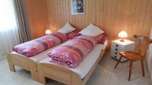 Ein Doppelbett mit floraler Bettdecke, zwei Nachttische mit Lampen, ein hölzerner Stuhl und ein Holz-Kopfteil.