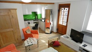 Un espacio habitable compacto con kitchenette, zona de comedor, televisor y cama.