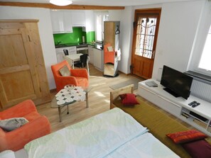 Ein gemütlicher, kompakter Wohnraum mit Küchenzeile, Essbereich, Fernseher und einem Bett.