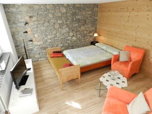 A room with a stone wall, wooden floor, a bed with pillows, a chair, a table with a glass bowl, and a lamp. - Studio Etana Studio, Dusche oder Bad, WC 2-Bettwohnung by Interhome (Zweisimmen)