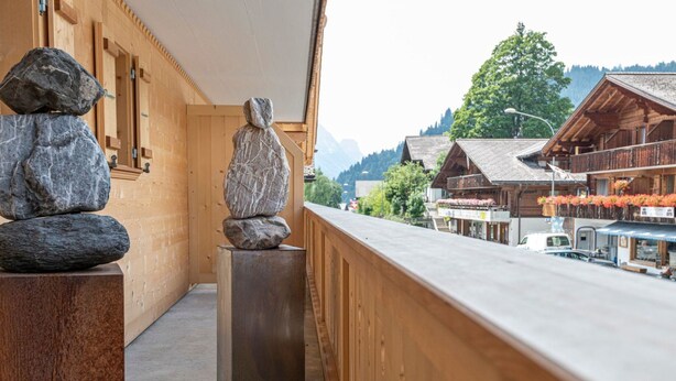Un balcón de madera con una escultura de piedra, vistas a un pueblo montañoso y edificios tradicionales de madera.