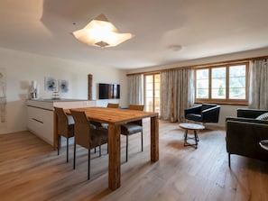 Ein stilvoller Wohnraum mit einem Holzespeisetisch, Stühlen, einer Couch und einem Fernseher.
