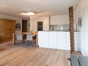 A modern kitchen with white cabinets, a wooden dining table, and chairs. - Grace Appartement/Fewo, Dusche oder Bad, WC, 1 Schlafraum 2-Bettwohnung by Interhome (Gstaad)