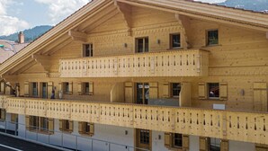 Un edificio de madera de varios pisos con balcones, ventanas amplias y un paisaje montañoso al fondo.