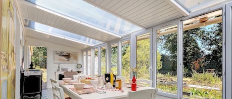 A dining area with a table set for four, surrounded by large windows offering a view of a garden.