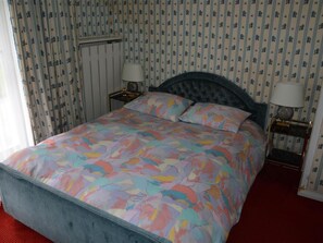 Ein Bett mit floralem Überwurf, zwei Nachttische inklusive Lampen sowie eine Wand mit Streifenmuster.