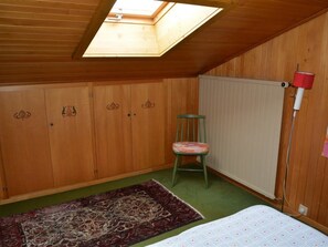 Een kamer met houten wanden, dakraam, radiator, stoel en bed.