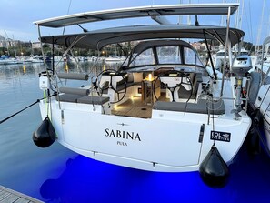 A white yacht named 'Sabina' docked at a marina with a helipad, a steering wheel, and a cabin area.