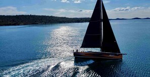 A sailboat on calm waters with a forested shoreline in the background. - Sibenik Sun-soaked Sailing: A Luxurious Croatian Voyage (Pirovac)