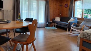 Een moderne woonkamer met houten vloer, een eettafel, een bank en een televisie.