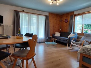 A modern living room with a wooden floor, a dining table, a sofa, and a TV. - Daheim Appartement/Fewo, Dusche oder Bad, WC 3-Bettwohnung by Interhome (Zweisimmen)
