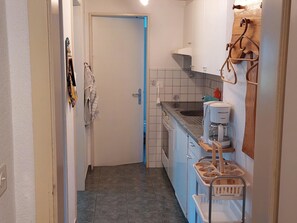 A compact kitchen with a sink, a coffee machine, and a stove. There is a door leading to another room. - Daheim Appartement/Fewo, Dusche oder Bad, WC 3-Bettwohnung by Interhome (Zweisimmen)