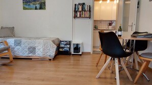 Een gezellige kamer met een bed, een bureau en een stoel. Er is een boekenplank en een klein tafeltje met een fles.