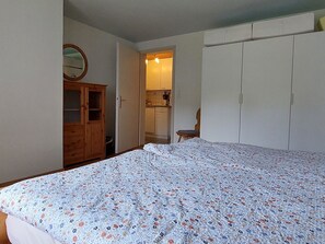 A bedroom with a bed, a wooden wardrobe, a mirror, and a kitchen area visible through an open door. - Daheim Appartement/Fewo, Dusche oder Bad, WC 3-Bettwohnung by Interhome (Zweisimmen)