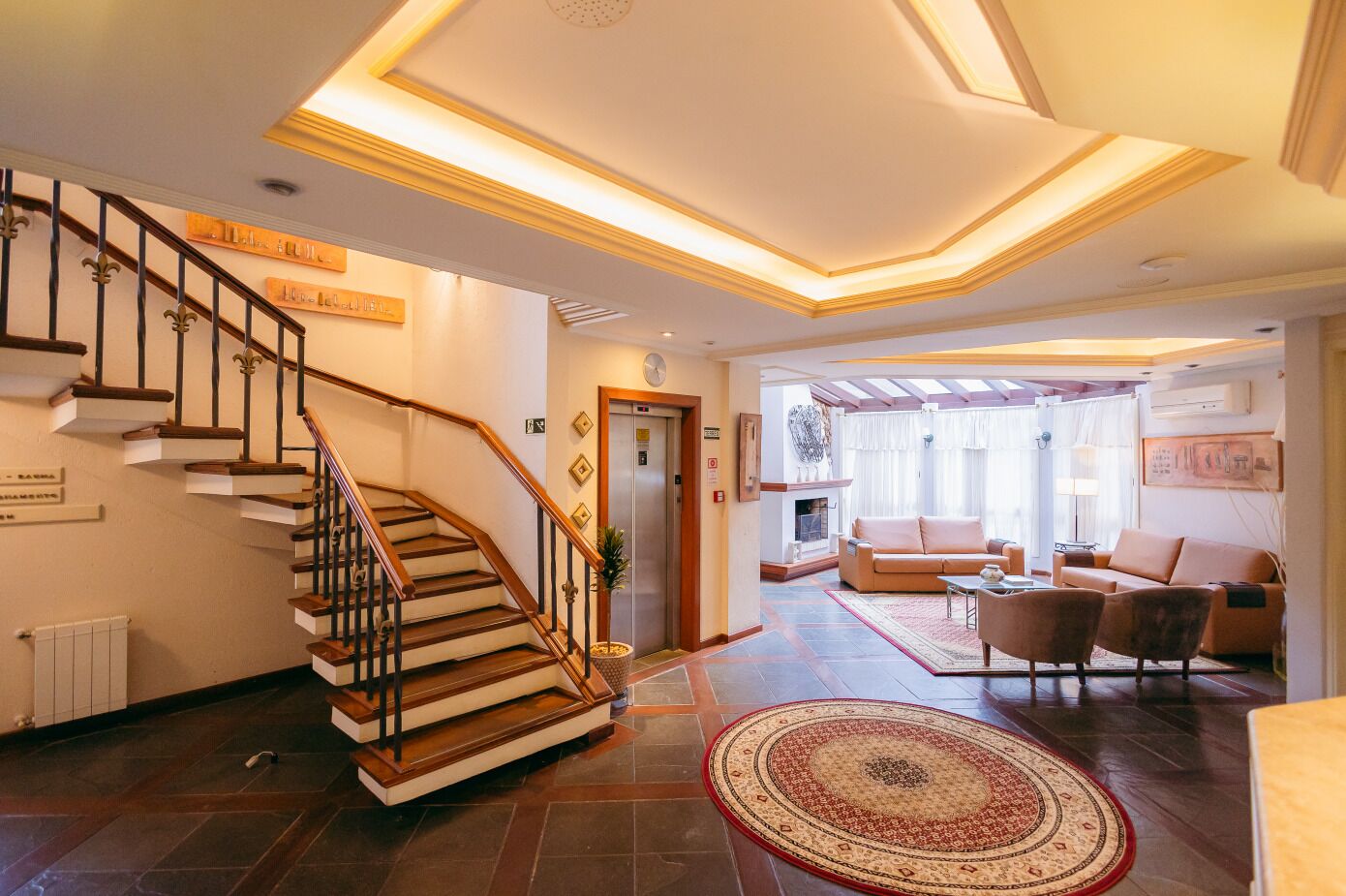 Una escalera con peldaños de madera y barandillas negras, una sala de estar con un sofá y sillones, y una chimenea.