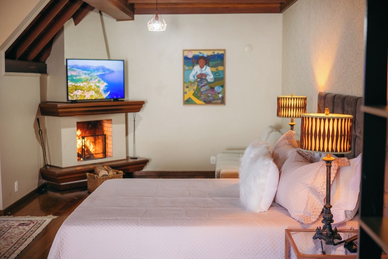 Un dormitorio con cama, televisor, chimenea y un cuadro en la pared.