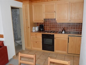A compact kitchen with wooden cabinets, a built-in oven, a coffee maker, and a sink. - Mireille Nr. 6 Appartement/Fewo, Dusche oder Bad, WC 2-Bettwohnung by Interhome (Gstaad)
