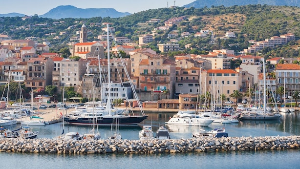 A marina with boats docked, surrounded by a town with buildings and a mountainous backdrop. - Sun-Kissed Sailing Adventure in Córcega (Propriano)