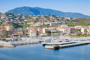 Puerto deportivo con barcos, muelle y edificios con montañas al fondo.