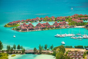 Un resort costero con varias edificaciones, un puerto deportivo con yates y un mar turquesa cristalino.
