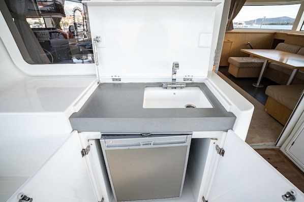 A compact kitchenette with a sink, a small refrigerator, and a dining area with a table and chairs. - Sibenik Sun-soaked Sailing: A Luxurious Croatian Voyage (Pirovac)