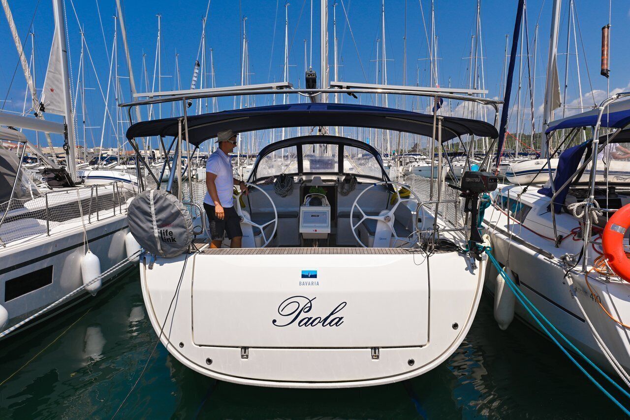Uma marina com barcos atracados, incluindo um barco branco chamado 'Paola' com toldo azul.