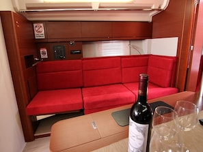 A compact interior with a red cushioned seating area, a table with a bottle and glasses, and a control panel with a no-smoking sign. - Sun-Kissed Sailing Adventure in Zadar, Croatia (Bibinje)