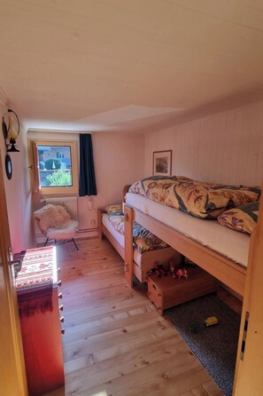 A cozy attic bedroom with a bunk bed, a chair, a radiator, and a window with a view. - Bachhüsi Appartement/Fewo, Dusche oder Bad, WC 6-Bettwohnung by Interhome (Zweisimmen)