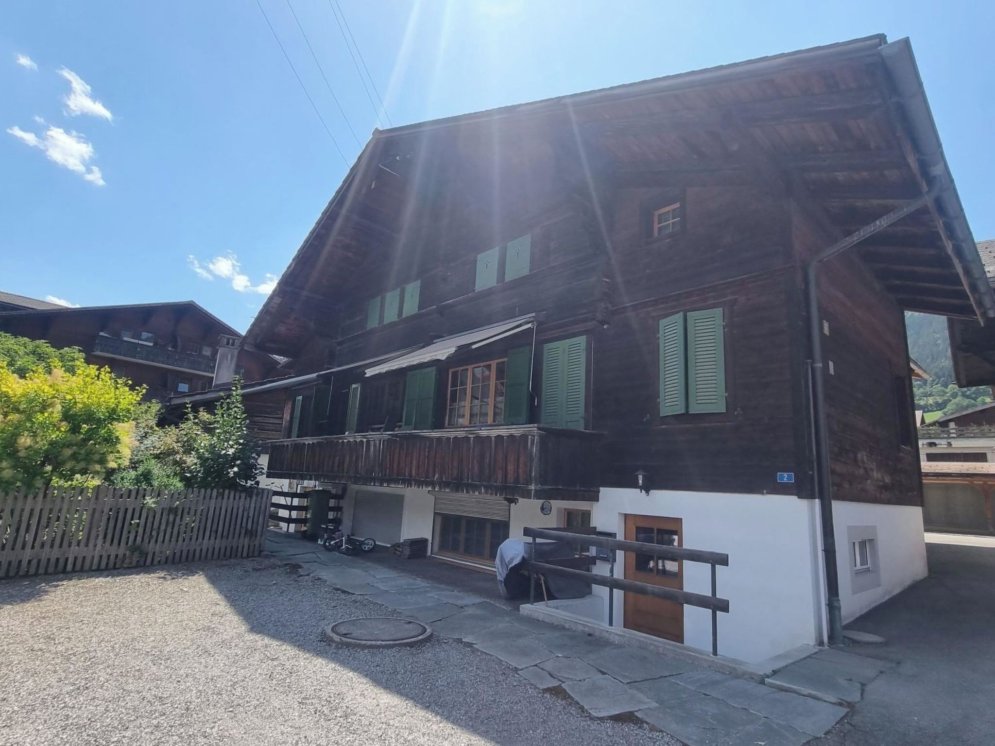 A two-story wooden house with a balcony, a small garage, and a wooden fence.