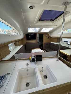 A compact galley with two sinks, a small seating area, and a TV mounted on the wall.