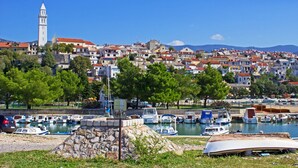 A coastal town with a prominent clock tower, a marina with boats, and densely packed buildings with red roofs. - Sun-Kissed Sailing Adventure in Northern Croatia (Novi Vinodolski)