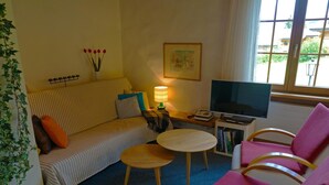 A cozy living room with a sofa, a small round table, a TV, and a bookshelf. - Zapfe (Küenzi) Appartement/Fewo, Dusche oder Bad, WC 6-Bettwohnung by Interhome (Gstaad)