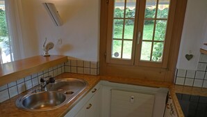 A small kitchen with a double sink, wooden countertop, white cabinets, and a window with a view of greenery. - Zapfe (Küenzi) Appartement/Fewo, Dusche oder Bad, WC 6-Bettwohnung by Interhome (Gstaad)