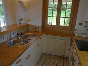 A small kitchen with a double sink, wooden countertop, white cabinets, and a window with a view of greenery. - Zapfe (Küenzi) Appartement/Fewo, Dusche oder Bad, WC 6-Bettwohnung by Interhome (Gstaad)