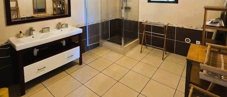 A bathroom with a double vanity, a glass shower enclosure, and a window with blinds.