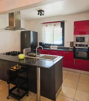 A compact kitchen with a central island, a gas stove, a microwave, and red cabinets. - Villa Ö Schandél (Saint-Paul)