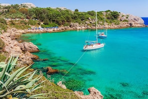 A coastal area with clear turquoise waters, rocky terrain, and a sailboat anchored near the shore.