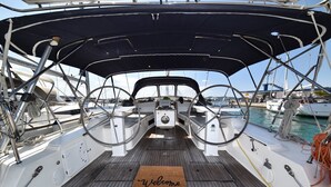 Dek van een boot met een 'Welcome' mat, stuurwiel en diverse bootbenodigdheden.