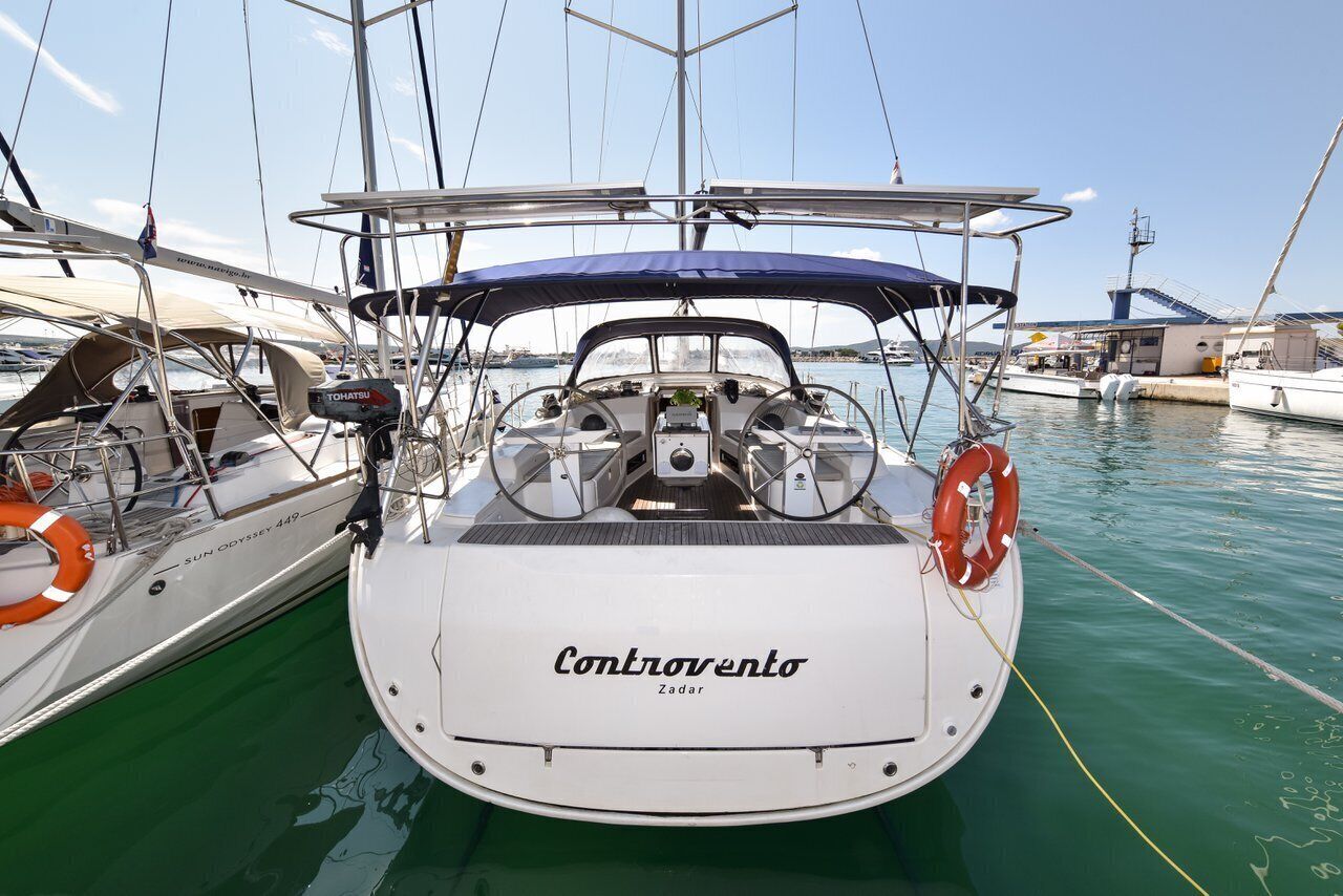 Een zeilboot genaamd 'Controvento' afgemeerd in een jachthaven, met andere boten, een heldere lucht en rustig water.