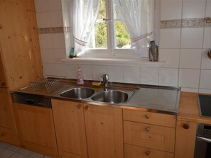 A kitchen with wooden cabinets, a double sink, and a window with curtains.